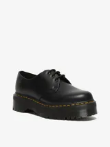 Zapato de cuero negro con plataforma gruesa y costuras amarillas. Tiene cordones negros y una puntera ancha y redondeada.