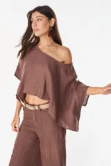 Blusa de lino italiano color blanco, con diseño holgado, escote asimétrico estilo off-shoulder y mangas cortas amplias.