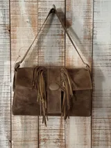 Cartera de cuero color marrón, con solapa frontal decorada con flecos y una hebilla metálica central, y correa ajustable para el hombro.