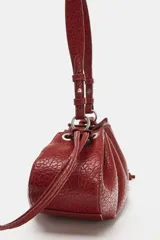 Mini bolso de hombro color bordó, con cuerpo fruncido, textura símil serpiente y tiras laterales ajustables. Cuenta con asa de hombro y cierre mediante fruncido.
