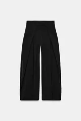 Pantalón de tiro medio de pierna ancha, color negro, con pliegues en el delantero y bolsillos laterales ocultos. Cierre frontal con cremallera, botón y ganchos metálicos.