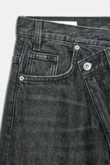 Jeans de tiro alto con diseño de pierna ancha y corte extra largo. Presenta una cintura cruzada asimétrica con cierre de cremallera y botones metálicos, además de un diseño clásico de cinco bolsillos.