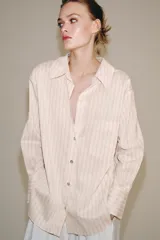 Camisa de mezcla de viscosa, color beige con rayas verticales rosadas, cuello solapa, manga larga con puños anchos, bajo redondeado y cierre frontal con botones.