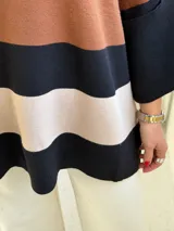 Poncho de tejido de punto con diseño de rayas horizontales anchas en tonos negro, marrón y beige, con cuello redondo y mangas amplias.