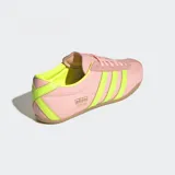 Championes Adidas modelo Tokyo de estilo retro, con exterior de nylon en color rosado y detalles en amarillo neón en las tres tiras laterales y el talón. Presenta una suela de caucho en tono marrón y un diseño de corte bajo.