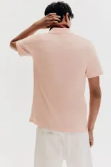 Remera polo color salmón de piqué de algodón, corte regular fit, con cuello clásico, tapeta de dos botones, mangas cortas y terminaciones acanaladas en cuello y mangas.