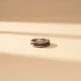 Anillo de diseño elegante elaborado en plata y oro, con una banda central incrustada de circonias pequeñas en tono oscuro.