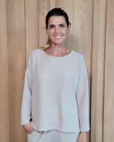 Remerón de textura acanalada en color gris claro, con cuello redondo, mangas largas y bolsillo frontal en el pecho. Presenta un diseño holgado con corte asimétrico, siendo más largo en la parte posterior.