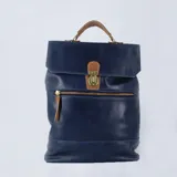 Mochila tipo portafolio de cuero azul con asa superior y correas ajustables color suela. Cierre frontal con hebilla y cierre trasero de seguridad.