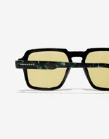 Lentes de sol Hawkers modelo Lash con armazón negro de frente cuadrado y patillas con estampado de mármol en tonos verdes. Presentan cristales amarillos y detalles metálicos en las esquinas.