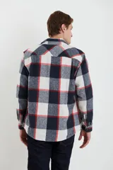 Sobrecamisa de tejido suave con diseño de cuadros en tonos azul marino, blanco y líneas rojas. Presenta cuello clásico, cierre frontal con botones, un bolsillo superior en el pecho y mangas largas con puños abotonados.