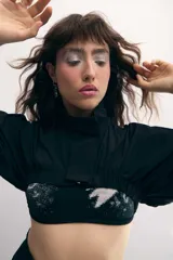 Campera cropped negra de tela técnica, con cuello alto, mangas murciélago y cierre frontal al tono.