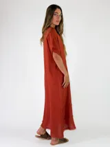 Vestido largo de lino color terracota, con escote en V y detalles de flecos en el cuello, mangas y en la parte inferior de la falda.