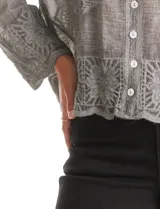 Camisa de algodón color gris con bordados florales en el frente y las mangas. Tiene cuello con solapa y cierre frontal con botones.