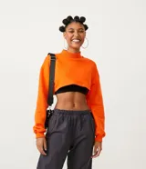Buzo cropped naranja de algodón, con cuello alto y ribete en los puños.