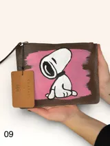 Sobre de cuero marrón con diseño pintado a mano que presenta al personaje Snoopy sobre un fondo rosado y la palabra 'heal'. Cuenta con cierre superior y etiqueta de cuero colgante.