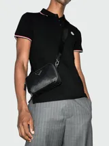 Polo de manga corta negro de piqué de algodón, con cuello y puños ribeteados en rojo, blanco y azul marino. Presenta un pequeño parche bordado en el pecho.