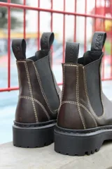 Bota Chelsea de cuero marrón con elásticos laterales negros, tiradores traseros y suela track negra.