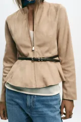 Chaqueta color beige con efecto ante, cuello redondo, manga larga y cierre frontal con cremallera. Presenta un bajo en evasé y un cinturón fino de cuero marrón oscuro con hebilla metálica.