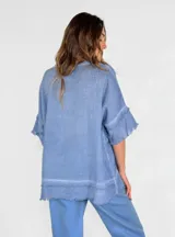 Blusa celeste de lino con escote en V y mangas cortas con volados. Tiene terminaciones desflecadas en el escote, mangas y ruedo.