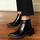 Botín de cuero vacuno color negro, con diseño combinado de cuero liso en la parte delantera y cuero con textura de reptil en el talón. Cuenta con un taco cuadrado de madera, cierre metálico en la parte posterior y suela de goma.