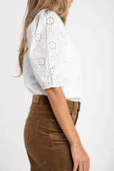 Remera de algodón color rosado con mangas cortas abullonadas de broderie con diseño floral calado. Presenta cuello redondo y costura vertical central en el frente.