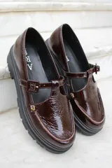 Zapato tipo guillermina en charol color bordó, con suela track negra, cierre de hebilla lateral y detalle de costura en el empeine.