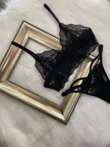 Conjunto de lencería de encaje negro compuesto por un top estilo bralette y una tanga colaless regulable. El top presenta breteles ajustables y diseño sin broches, confeccionado en encaje suave y elastizado.