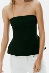 Top negro de tejido satinado, sin tirantes y con escote recto. Presenta costuras marcadas y diseño con peplum en la parte inferior, con cierre de cremallera oculta en la espalda.