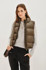 Chaleco acolchado de corte corto, color verde oliva, con cuello alto ajustable mediante cordones elásticos y cierre frontal con cremallera.