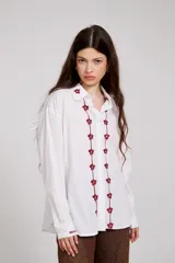 Camisa blanca de corte holgado con cuello camisero y cierre frontal de botones. Presenta un delicado bordado vertical de flores pequeñas en color bordó a lo largo de la botonera y en el cuello.