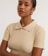 Blusa polo beige de manga corta, confeccionada en tejido canelado de rib de algodón con elastano, que proporciona un ajuste cómodo y una caída ajustada.