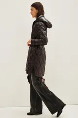 Campera puffer larga de color negro con diseño acolchado en forma de rombos. Cuenta con capucha, cierre frontal, bolsillos con cierre y un cinturón elástico con hebilla metálica en la cintura.