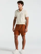 Chomba color crema de manga corta con cuello clásico y logo bordado en el pecho. Detalles de rayas en cuello y mangas.