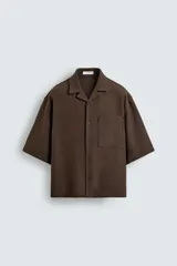 Camisa de corte boxy fit confeccionada en tejido con lino, color negro. Presenta cuello bowling, manga corta y un bolsillo plastrón en el pecho con cierre frontal de botones.