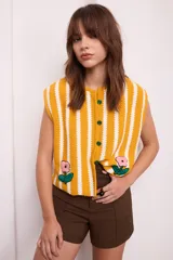 Chaleco tejido a crochet con rayas verticales amarillas y blancas, cierre frontal con botones verdes y bordados artesanales de flores rosadas con tallos verdes en la parte inferior.