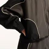 Campera New Balance Trackside de color gris oscuro, con cuello alto, cierre frontal completo y ribetes blancos en contraste. Cuenta con el logo de la marca bordado en el pecho.