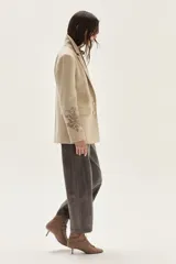 Blazer de paño color beige, con solapas clásicas y bordados decorativos en tono más oscuro en la parte inferior de las mangas.