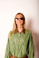 Camisa verde de cuero sintético con cuello marrón, cierre frontal con botones, dos bolsillos con solapa en el pecho y cinturón marrón.
