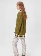 Cardigan de punto trenzado en color negro con detalles en color crema en los bolsillos, puños y ruedo. Presenta un diseño oversize, cierre frontal con botones y bordado decorativo en uno de los bolsillos delanteros.