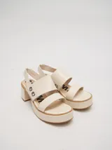 Sandalias de plataforma con taco cuadrado de 6 cm y base de 3 cm. Presentan dos tiras anchas en el empeine con detalles de doble argolla metálica en los laterales y una correa trasera con elástico para mayor ajuste.