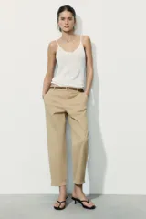 Pantalón chino color beige de tiro medio con bolsillos frontales y falsos bolsillos de vivo en la espalda. El bajo tiene un acabado con vuelta. Incluye un cinturón trenzado marrón.