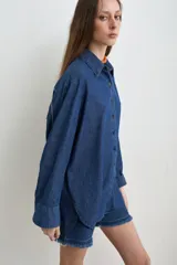 Camisa de jean azul, de corte holgado y manga larga, con cuello camisero y cierre frontal de botones oscuros.