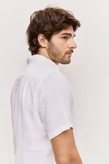 Camisa de manga corta en color blanco, con cuello clásico y cierre frontal de botones al tono. Presenta un diseño versátil de corte regular y textura liviana, ideal para looks frescos.