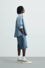 Bermuda de denim de algodón, color azul medio lavado, de corte ancho (baggy fit) y largo hasta la rodilla. Presenta cinco bolsillos y cierre frontal con cremallera y botón.