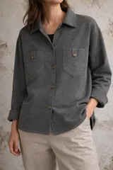 Camisa de tejido de lana color gris oscuro, con cuello clásico, cierre frontal de botones y dos bolsillos delanteros con solapa y botón.