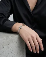 Pulsera rígida abierta de acero plateado, con diseño minimalista que presenta dos triángulos en los extremos.