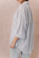 Camisa lila oversize de algodón con bordado floral calado tipo broderie, cuello camisero, manga larga y abotonadura frontal.
