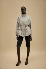 Chaqueta de corte holgado con estampado de cuadros, cuello subido, manga larga con puños elásticos y cintura ajustable mediante cordones. Presenta bolsillos delanteros con solapa y cierre frontal con cremallera oculta y botones a presión.