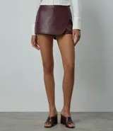 Short pollera de tiro alto confeccionado en poliuretano con acabado liso. Presenta un diseño cruzado en el frente, cierre posterior con cremallera y corte ajustado.